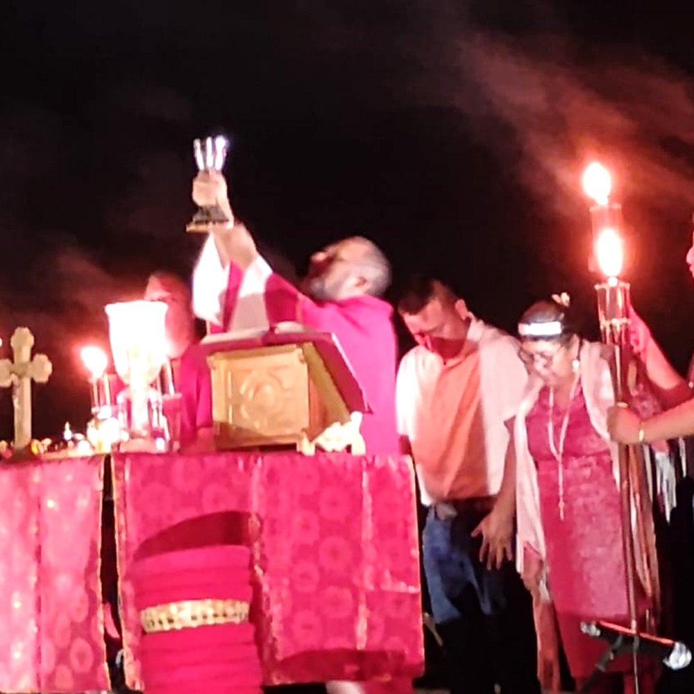 The priest raises the chalice at the altar during the 2025 Pentecost Vigil at the Mission, among torches