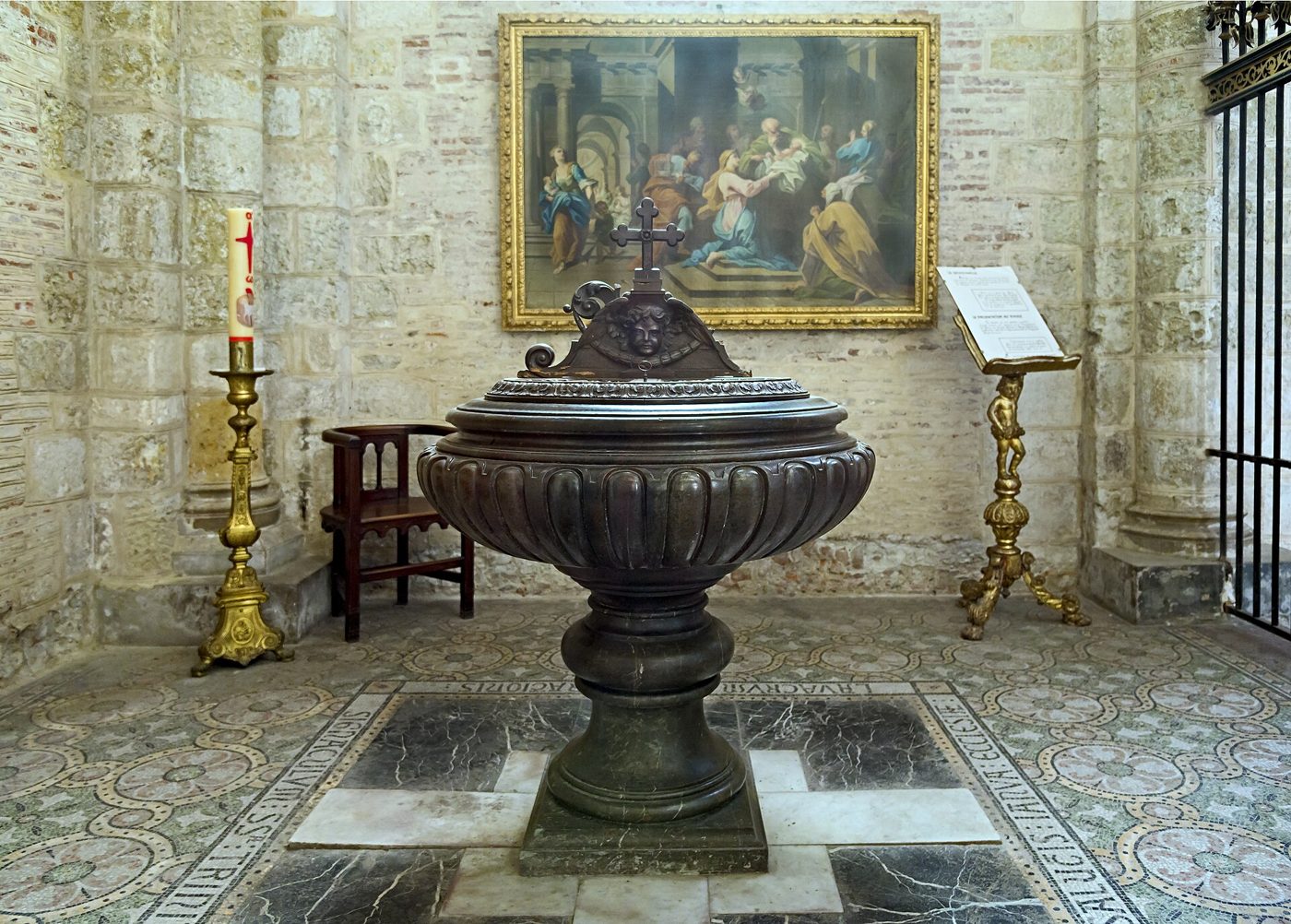 Bronze baptismal font next to a candle, in a church