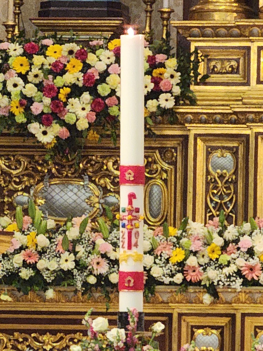 Paschal candle among flowers, in front of a golden altar